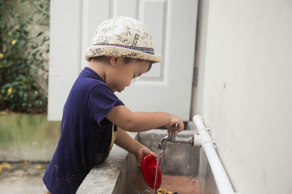 small child wearing a hat and filling a bucket with water