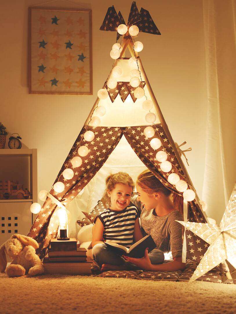 Mother and daughter in a fairy light lit tent in a bedroom