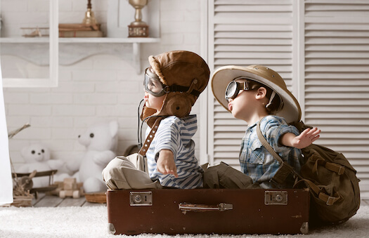 Two children are playing dressup as pilots, flying in a cardboard box