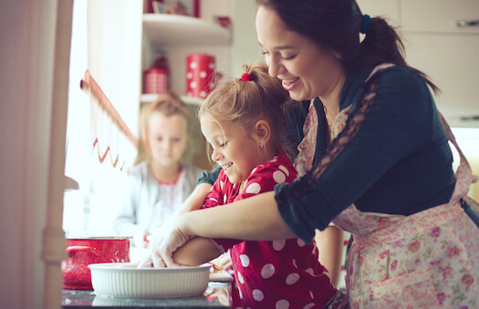 A woman helps a child mix a baking cake mix in a ceramic bowl in a kitchen